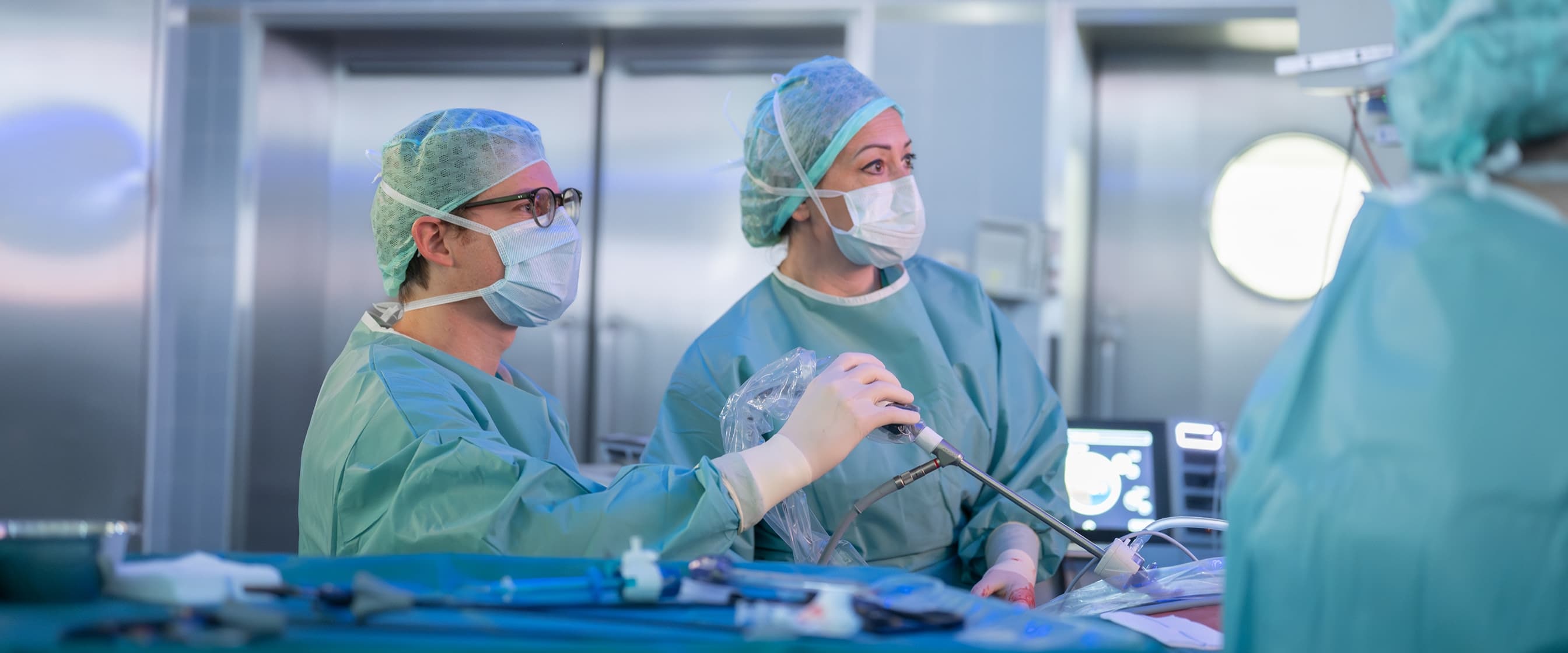 Eine Ärztin und ein Arzt blicken während einer OP konzentriert auf den Bildschirm