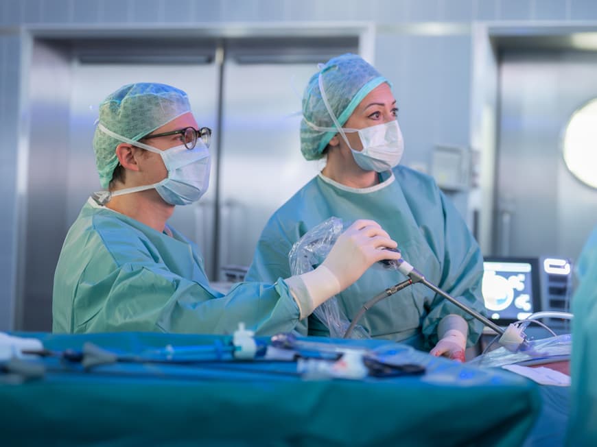 Eine Ärztin und ein Arzt blicken während einer OP konzentriert auf den Bildschirm