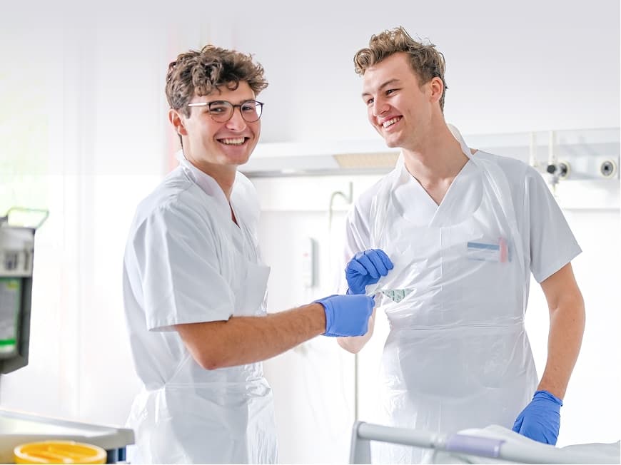 Zwei Pflegeazubis sind auf Station, einer davon blickt in die Kamera