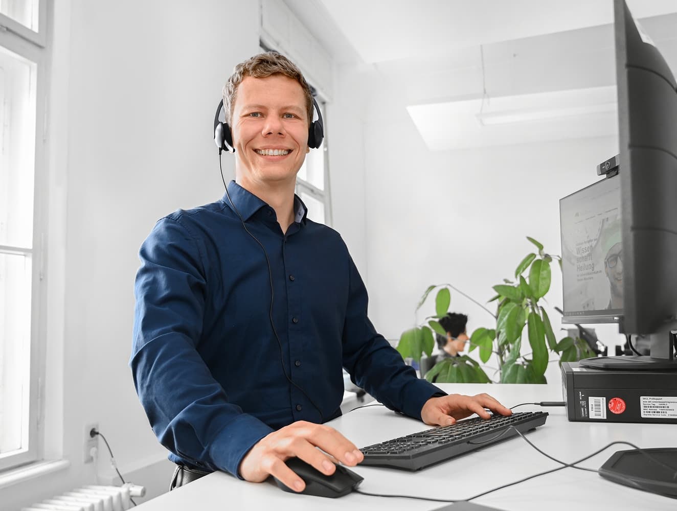 Ein IT-Mitarbeiter steht an seinem Schreibtisch und blickt während eines Calls in die Kamera