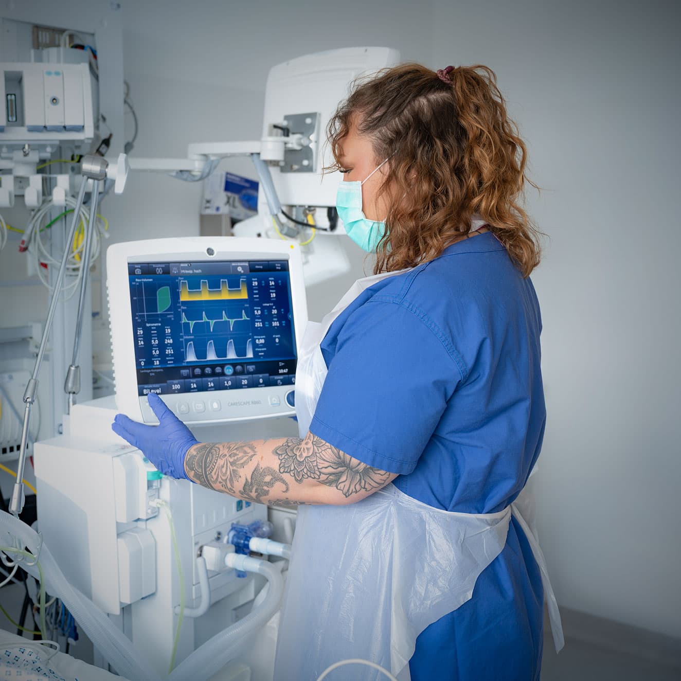 Eine Intensivpflegefachkraft steht am Patientenbett an der Beatmungsmaschine