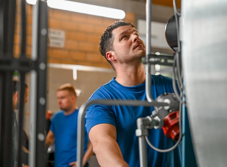 Ein Elektroniker prüft eine Maschine im Keller des TUM Klinikums. Zwei Kollegen stehen im Hintergrund und besprechen etwas.
