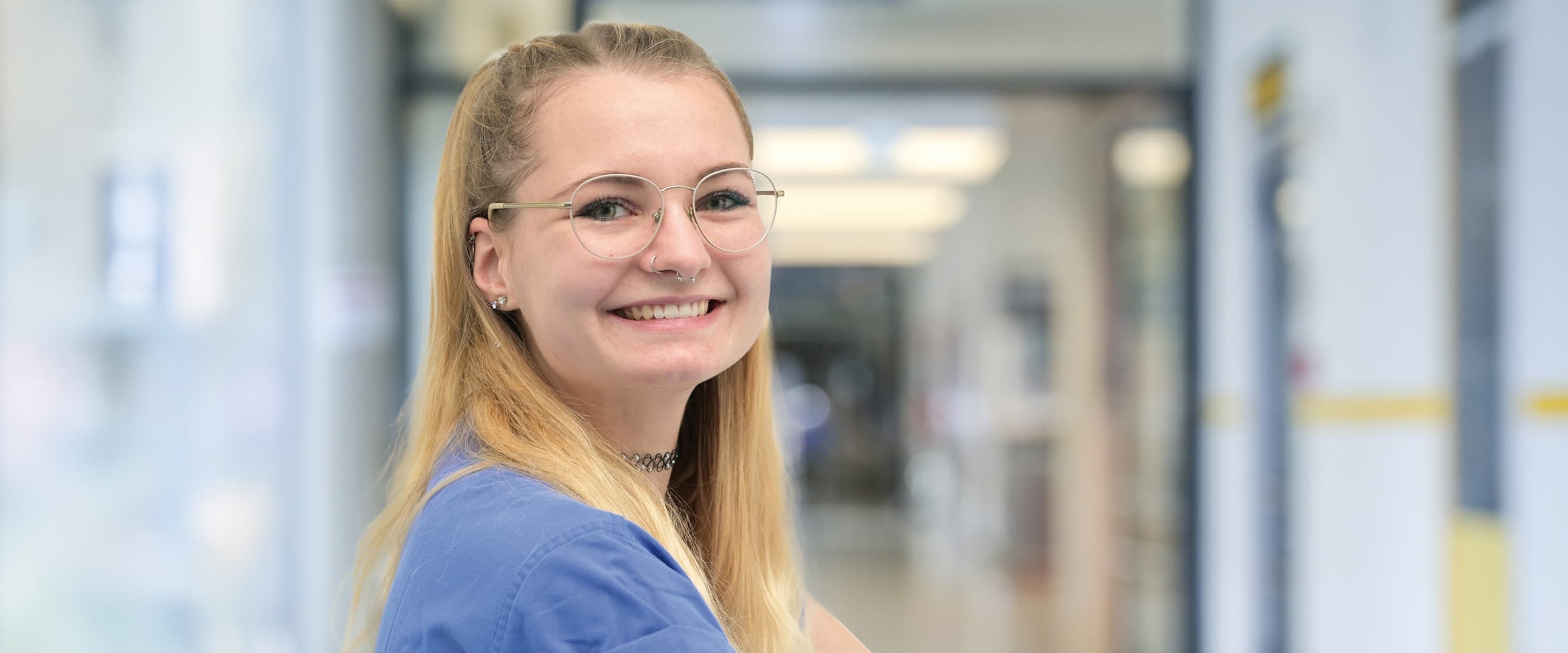 Eine Praktikantin steht auf dem Krankenhausflur und blickt in die Kamera