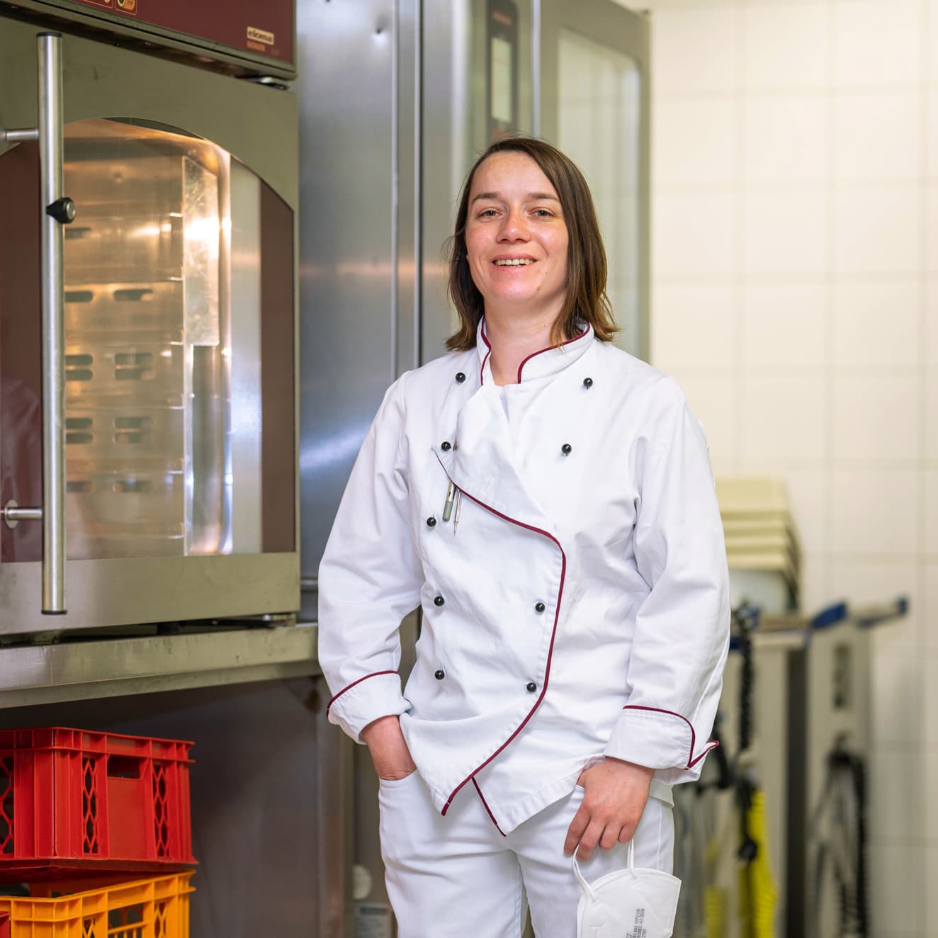 Eine Köchin steht vor einem Ofen und blickt stolz in die Kamera