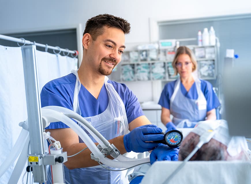 Eine Pflegefachfrau steht am Krankenbett auf der Intensivstation und versorgt den Patienten