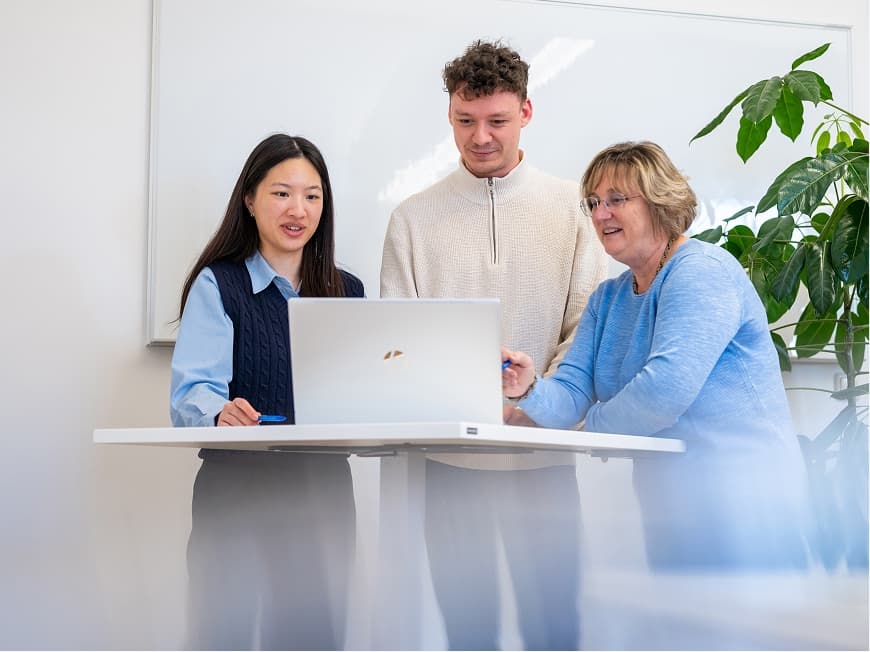 Drei Mitarbeitende aus der Verwaltung stehen an einem Stehtisch und besprechen ein Projekt am Laptop