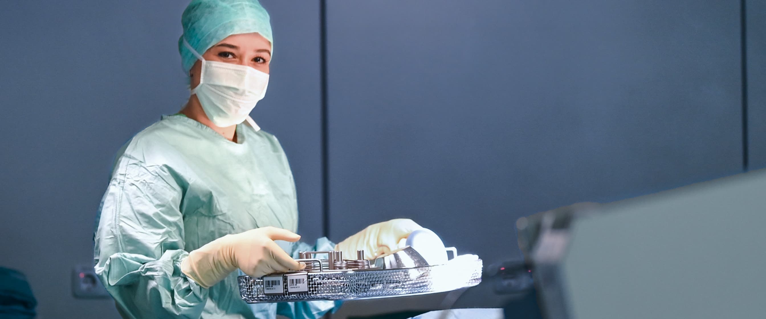 Eine Auszubildende zur Operationstechnischen Assistentin hält ein OP-Instrumente-Set während einer OP und blickt in die Kamera