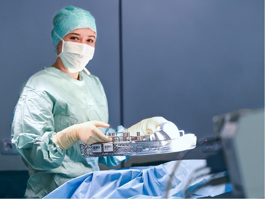 Eine Auszubildende zur Operationstechnischen Assistentin hält ein OP-Instrumente-Set während einer OP und blickt in die Kamera