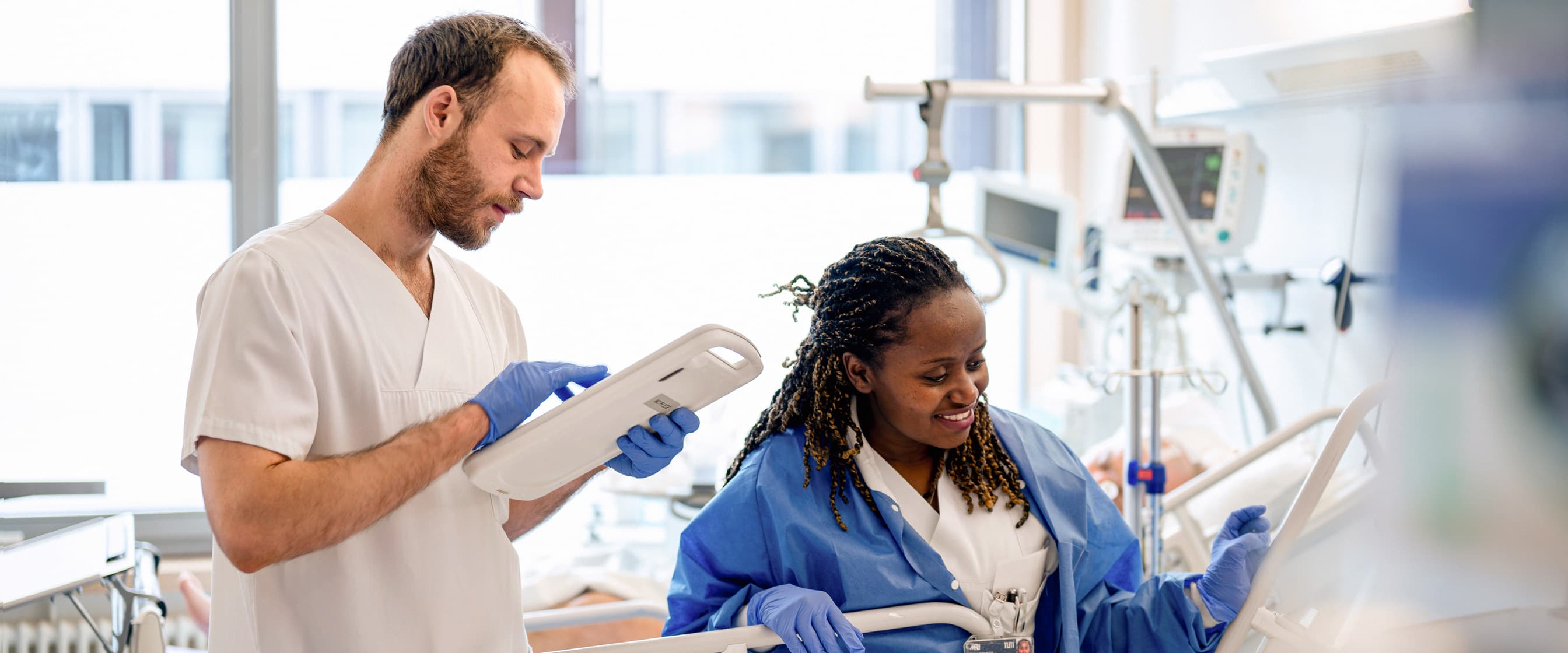 Ein Pflegefachmann und eine Pflegefachfrau versorgen einen Patienten auf Station