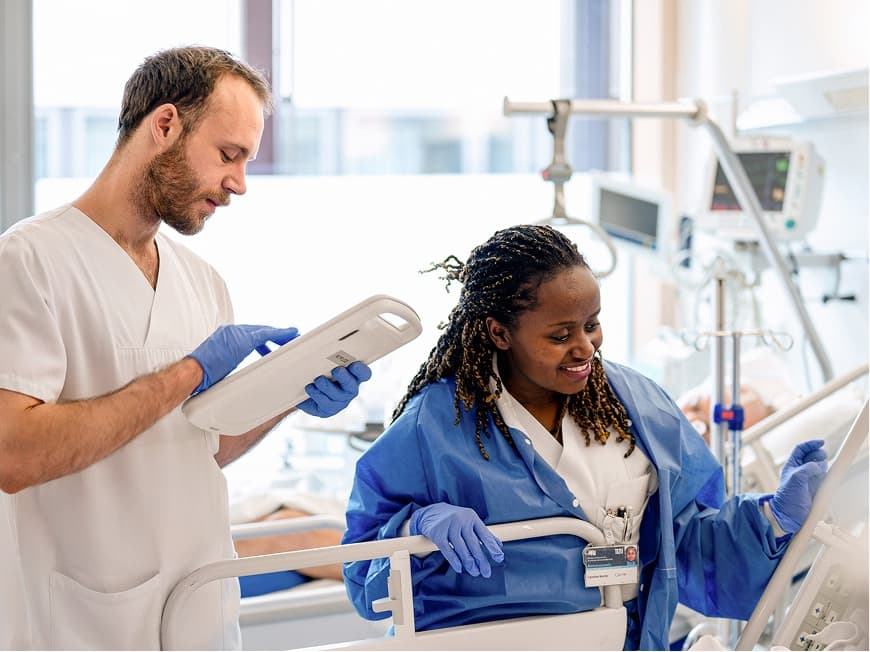 Ein Pflegefachmann und eine Pflegefachfrau stehen am Patientenbett und versorgen den Patienten