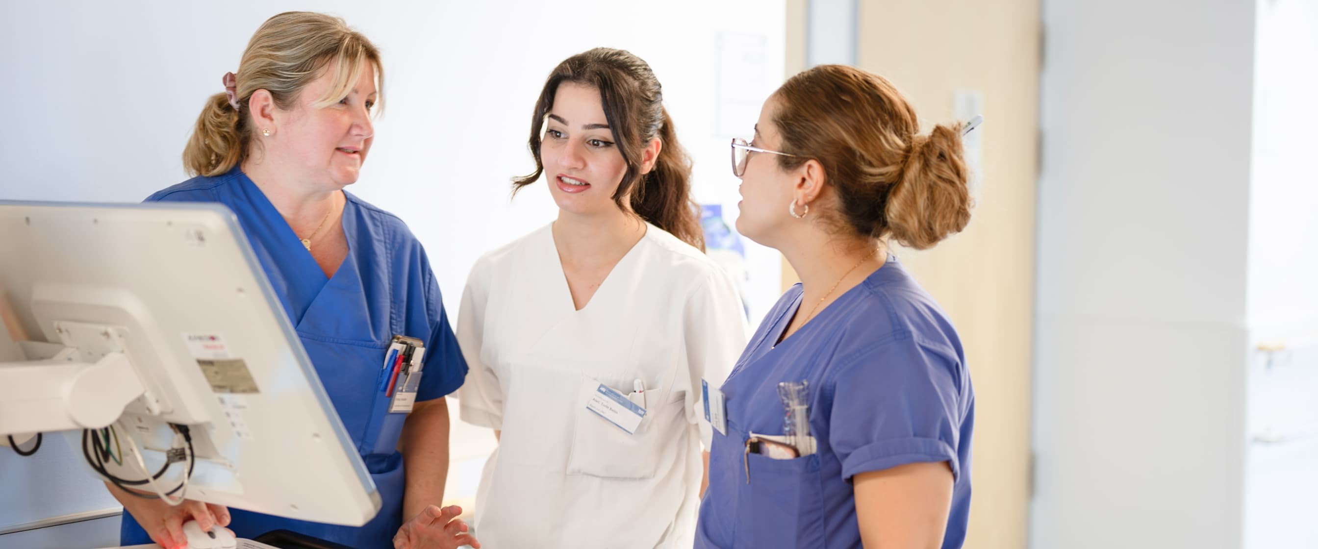 Zwei Auszubildende zur Pflegefachfrau bekommen von einer Praxisanleiterin etwas erklärt