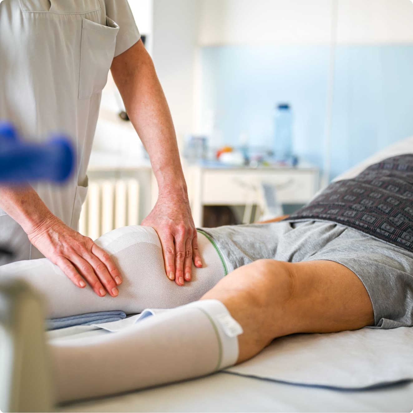 Eine Physiotherapeutin behandelt das Knie eines frisch operierten Patienten am Patientenbett