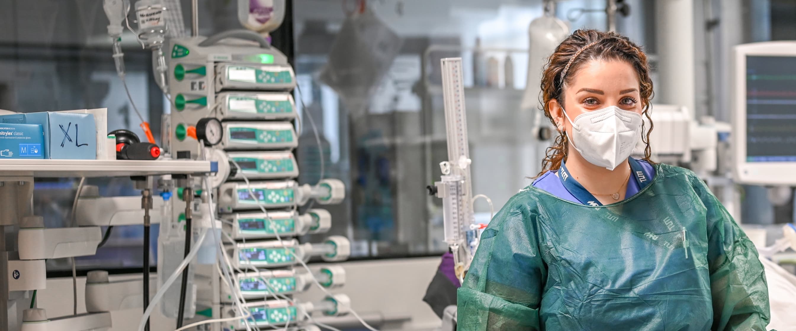 Eine Intensivpflegefachfrau steht im Patientenzimmer und blickt in die Kamera