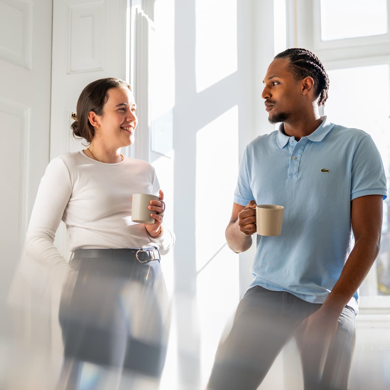 Ein Dualer Student spricht mit der Ansprechpartnerin für Duale Studenten, beide stehen mit einer Tasse Kaffee auf dem Flur