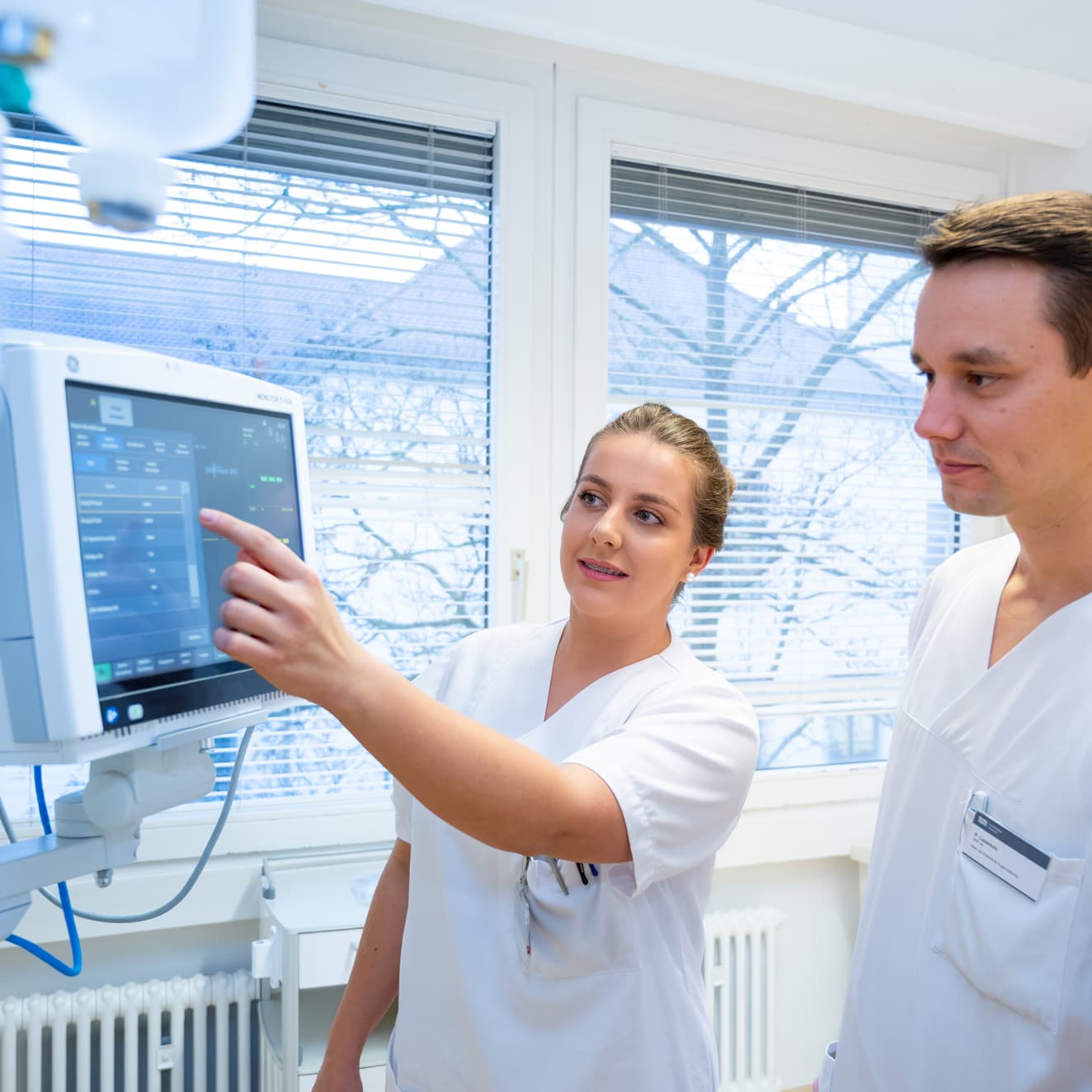 Eine Pflegefachfrau erklärt einem Pflegestudierenden etwas am Überwachungsmonitor