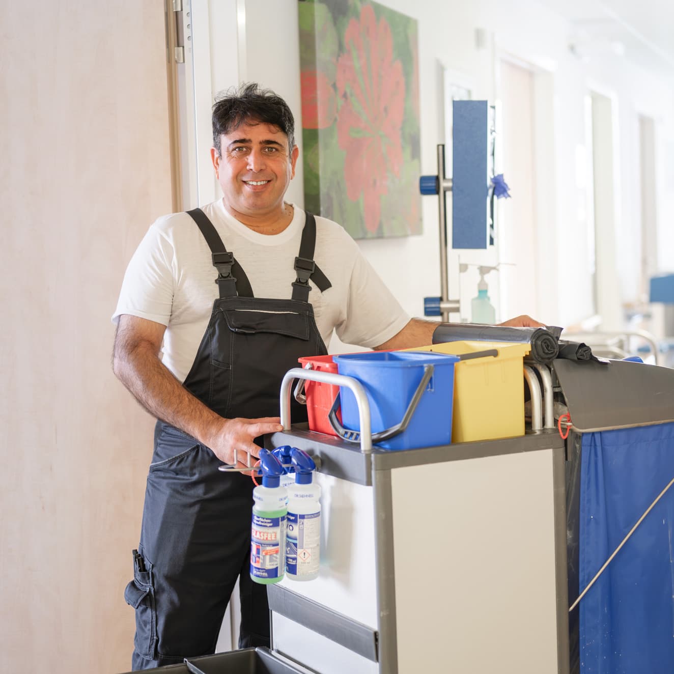 Eine Putzfachkraft steht mit einem Putzwagen auf einem Stationsgang
