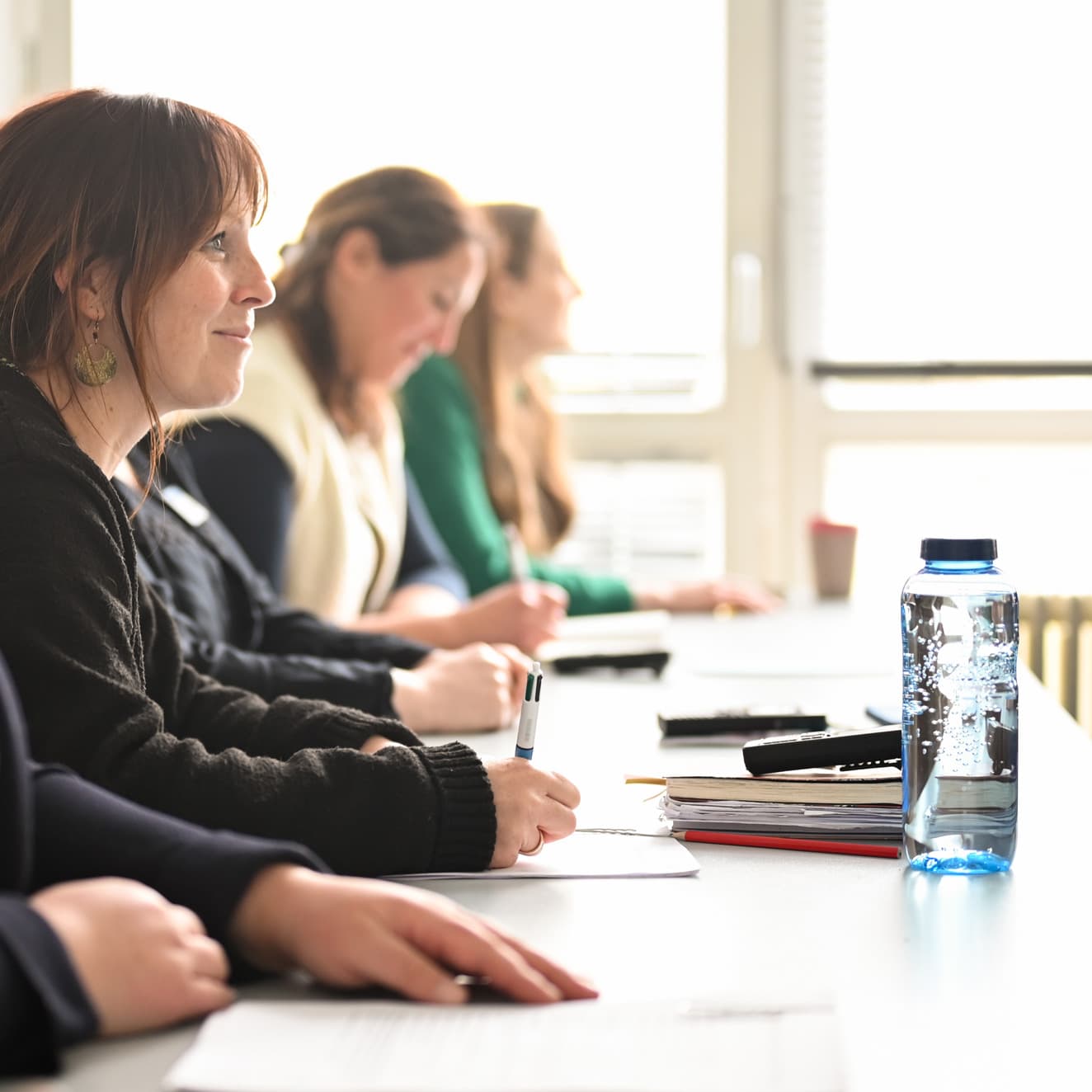 Mehrere Pflege-Studierende sind seitlich zu sehen, wie sie an einem langen Schultisch sitzen.