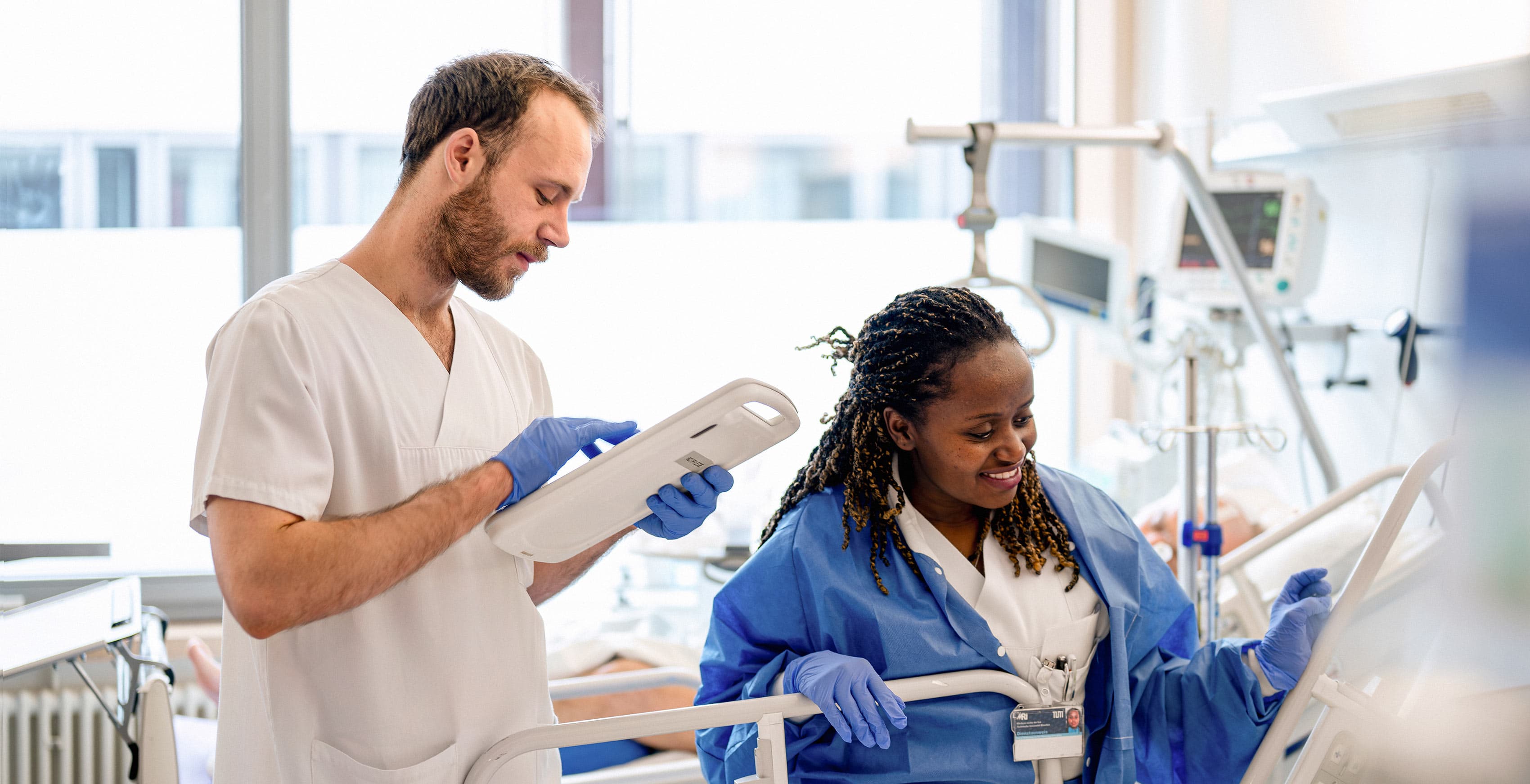 Zwei Pflegefachkräfte versorgen einen Patienten am Patientenbett